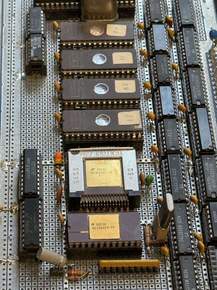 Component side of the wire-wrapped NS32032 audio computer: the NS32032 CPU and NS32201 timing control unit in ceramic packages among rows of logic ICs and four EPROMs on perfboard.